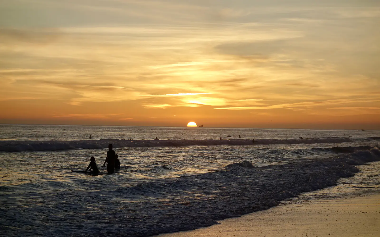 Surferi u plićaku na plaži Carcavelos u zalazak sunca